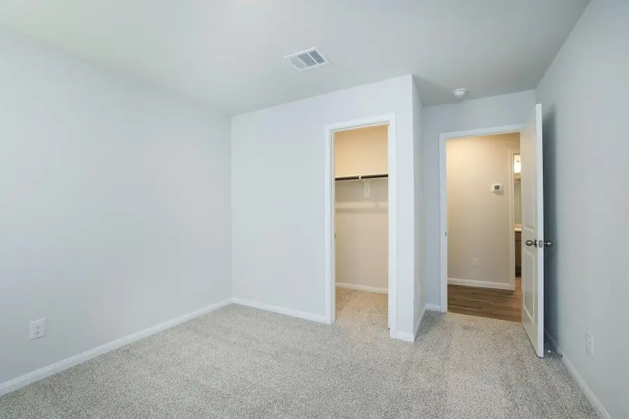 The walk-in closet provides ample storage and an open door leads to a hallway. The room is well-lit and has a simple, clean design.
