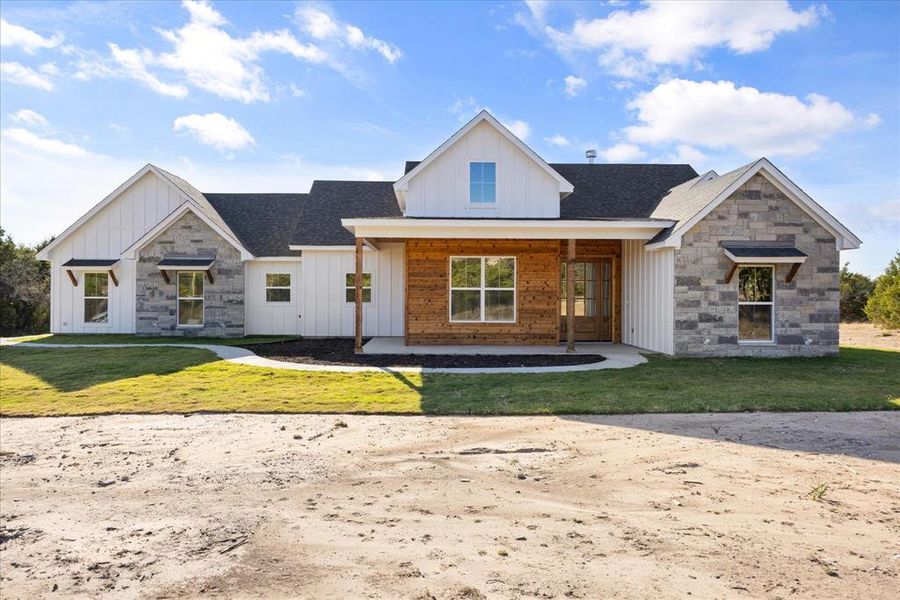 Modern inspired farmhouse with stone siding, board and batten siding, a front yard, and covered porch