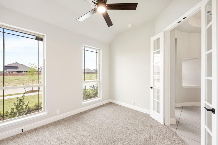 Empty bedroom with carpet, ceiling fan, large windows, and white French doors Empty bedroom with carpet, ceiling fan, large windows, and white French doors