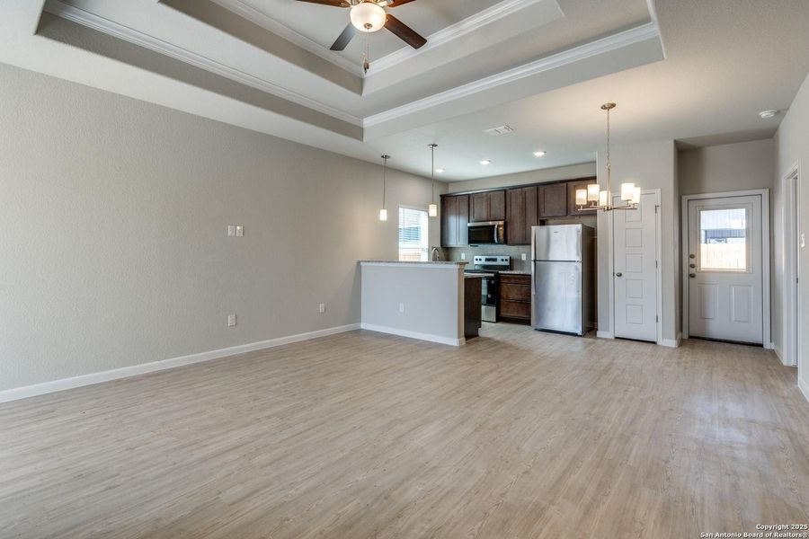 Open-concept living area featuring wood-finish flooring, a tray ceiling with a ceiling fan, and recessed lighting