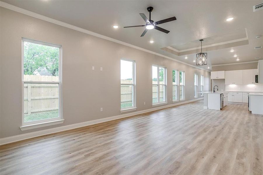 Unfurnished living room featuring a sink, ornamental molding, a tray ceiling, and light wood-type flooring Unfurnished living room featuring a sink, ornamental molding, a tray ceiling, and light wood-type flooring