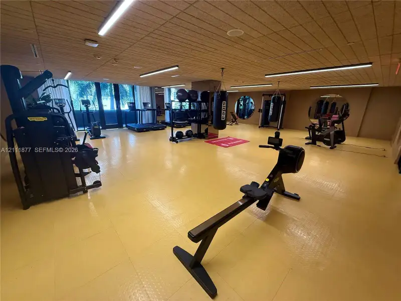 Fitness center featuring wood-paneled ceilings, linear LED lighting, circular wall mirrors, and textured industrial-style flooring