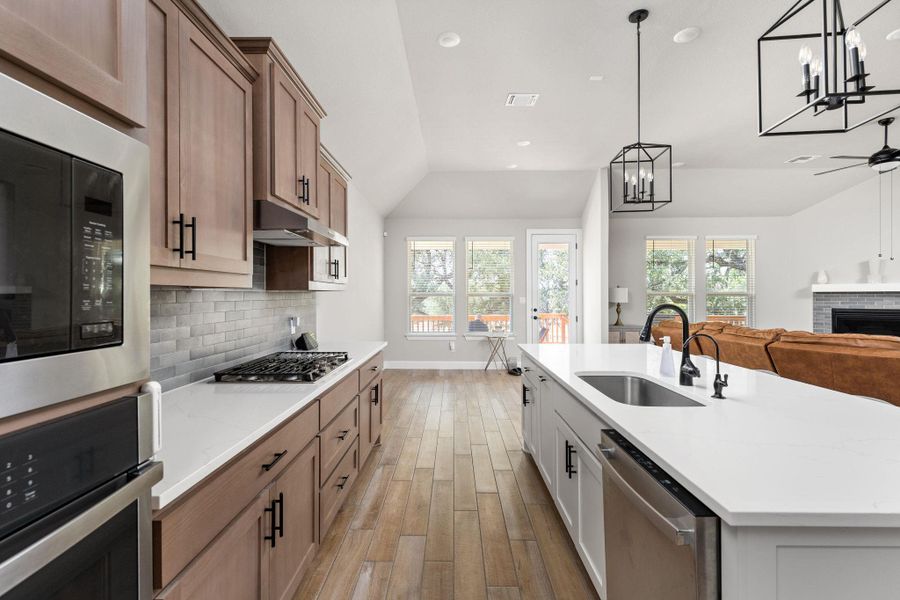 Kitchen featuring dual tone cabinets, stainless steel appliances, vaulted ceiling, open floor plan, and wood tiled floors