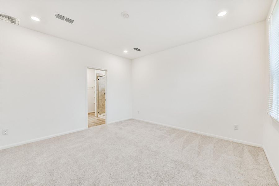 Primary bedroom boasts plenty of natural lighting, neutral carpet, recessed lighting and high ceilings.