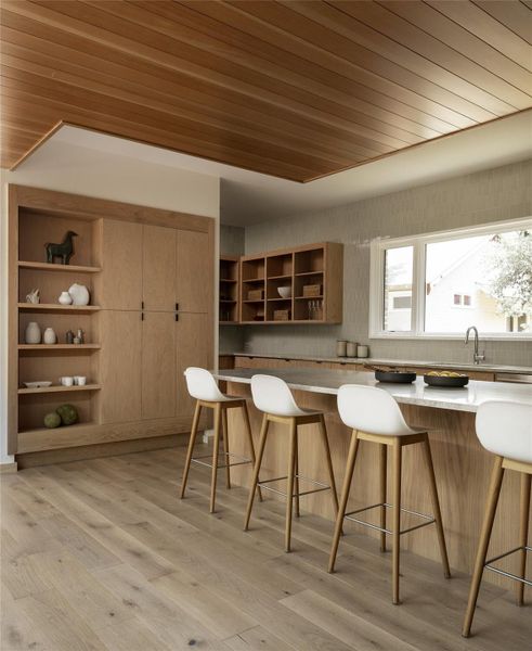 Kitchen with wooden ceiling, light countertops, light wood finished floors, open shelves, and a breakfast bar area