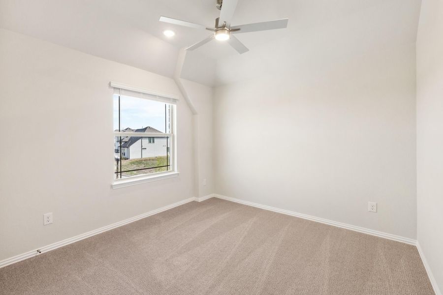 Empty bedroom with vaulted ceiling, ceiling fan, carpet flooring, and single window with neighborhood view Empty bedroom with vaulted ceiling, ceiling fan, carpet flooring, and single window with neighborhood view