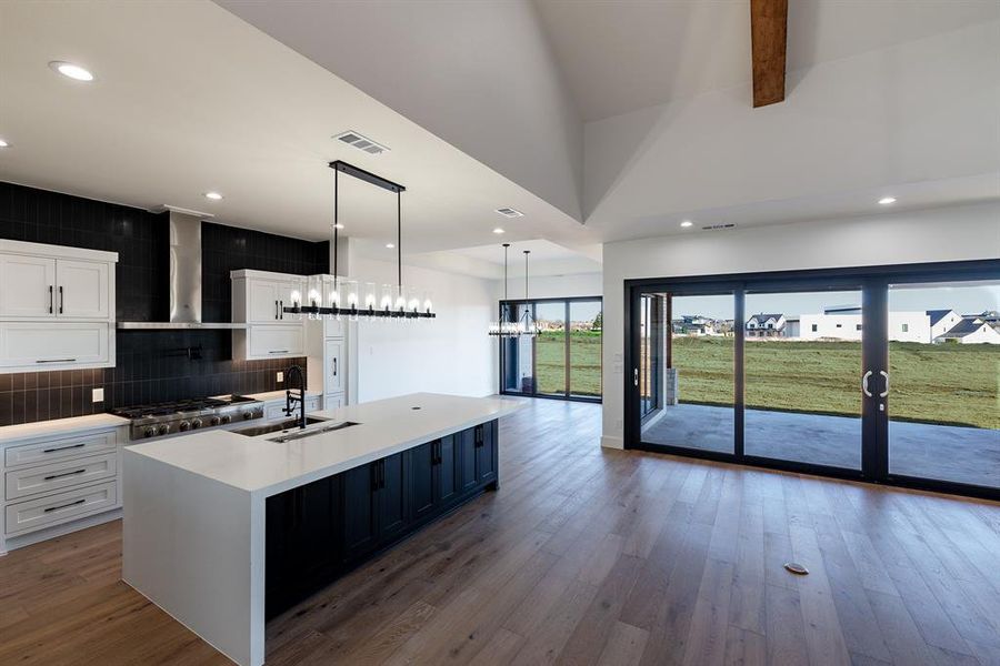 Kitchen featuring pendant lighting, an island with sink, sink, white cabinets, and wall chimney exhaust hood