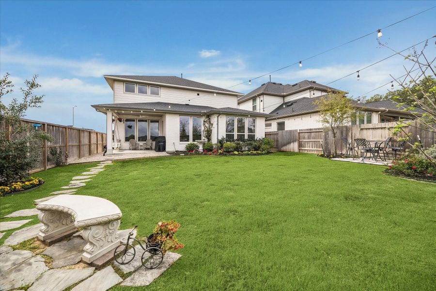 From this angle, the backyard showcases a cozy area for a table and chairs with string lights stretching from the home to the fence line, creating the perfect setting for outdoor gatherings.