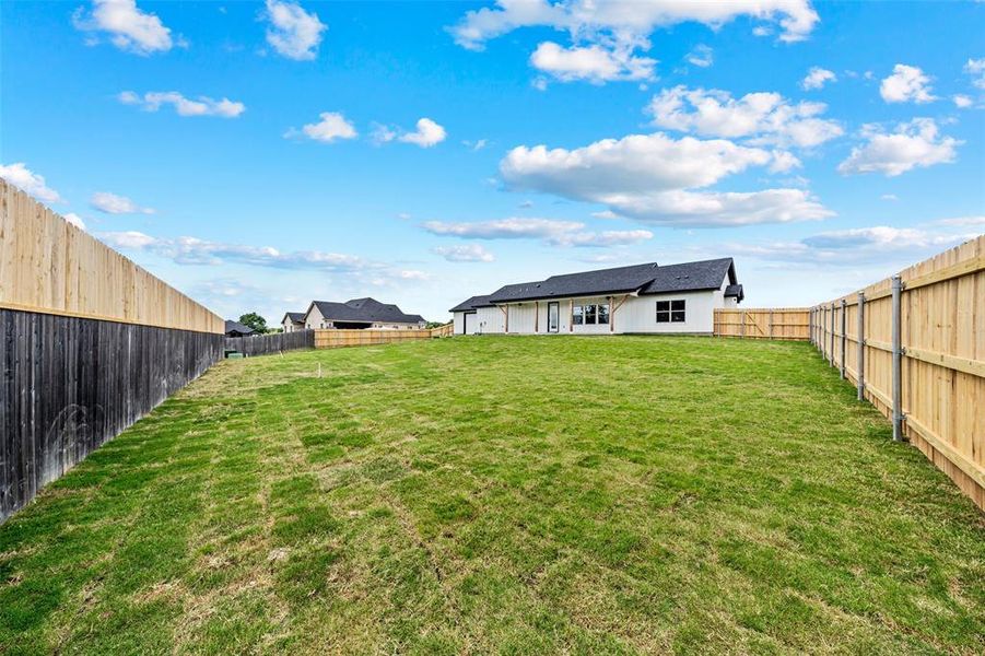 Expansive backyard featuring a lush lawn, new wood privacy fencing, and a white exterior residence with dark-framed windows Expansive backyard featuring a lush lawn, new wood privacy fencing, and a white exterior residence with dark-framed windows