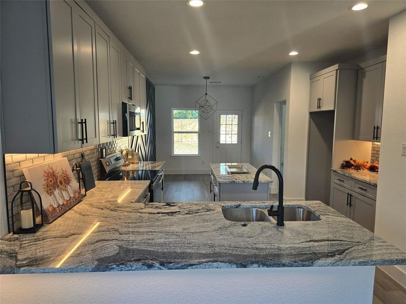 Kitchen with light stone counters, tasteful backsplash, appliances with stainless steel finishes, recessed lighting, and dark wood-type flooring Kitchen with light stone counters, tasteful backsplash, appliances with stainless steel finishes, recessed lighting, and dark wood-type flooring