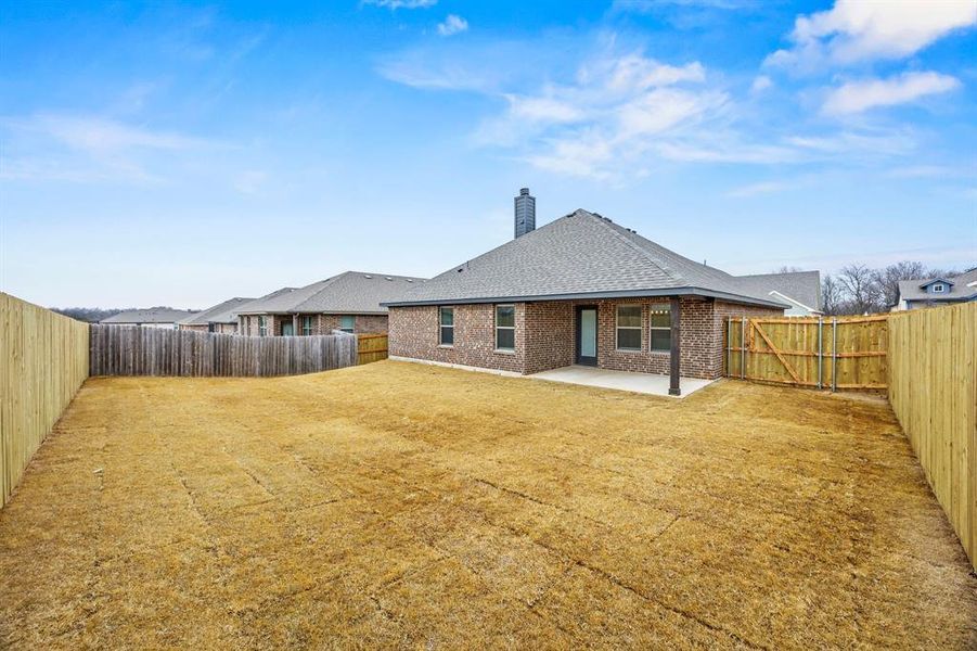 Back of house with brick siding, a shingled roof, a patio, and a fenced backyard