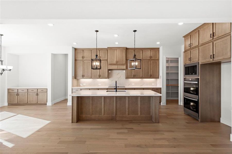 Kitchen featuring stainless steel microwave, light hardwood / wood-style floors, a kitchen island with sink, and hanging light fixtures