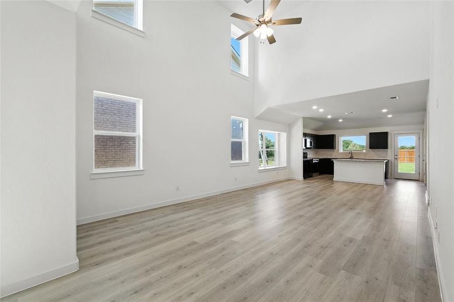 Unfurnished living room featuring healthy amount of natural light, ceiling fan, light wood-style flooring, and a high ceiling Unfurnished living room featuring healthy amount of natural light, ceiling fan, light wood-style flooring, and a high ceiling