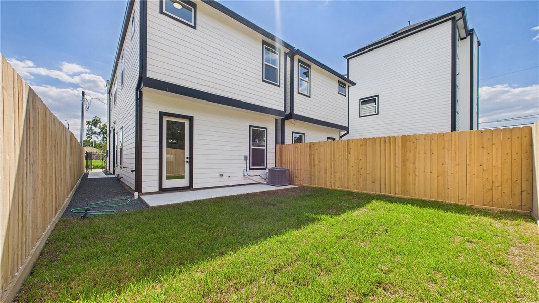This is a modern two-story home with clean, white siding and black trim. The backyard features a small, well-maintained lawn, a concrete patio, and is enclosed by a wooden privacy fence. Perfect for outdoor relaxation. This is a modern two-story home with clean, white siding and black trim. The backyard features a small, well-maintained lawn, a concrete patio, and is enclosed by a wooden privacy fence. Perfect for outdoor relaxation.