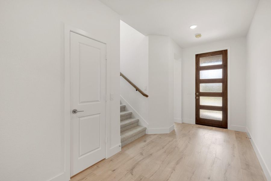 Entryway with wood front door with glass panels, staircase, and light hardwood floors in white-walled foyer