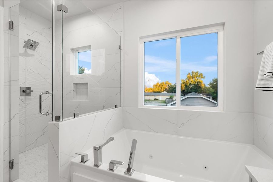 A large jetted soaking tub and frameless glass shower await after a long day, complete with a thoughtfully designed shampoo niche and sleek chrome fixtures for a touch of modern luxury. A large jetted soaking tub and frameless glass shower await after a long day, complete with a thoughtfully designed shampoo niche and sleek chrome fixtures for a touch of modern luxury.