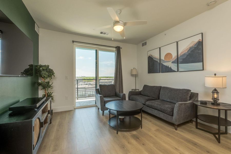 The living space features light wood-look flooring, a ceiling fan, and sliding glass doors leading to an outdoor area
