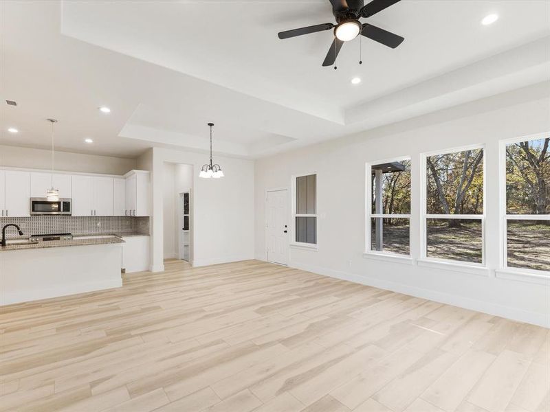 Unfurnished living room with a tray ceiling, ceiling fan, light wood finished floors, and hanging lights