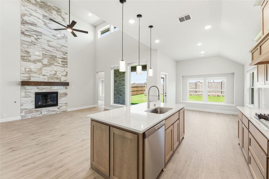 Open kitchen with island, quartz countertop, and stone fireplace under vaulted ceiling with pendant lights