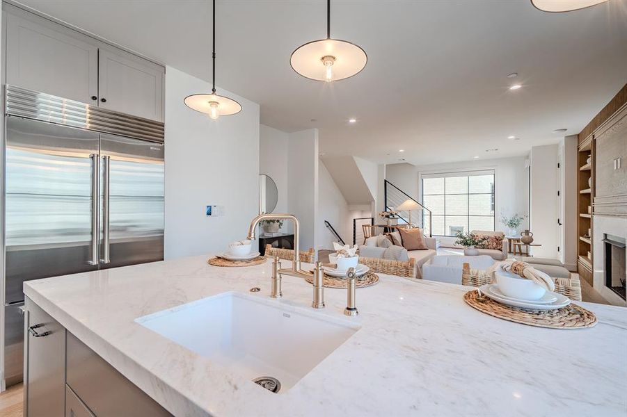 Kitchen with light stone countertops, a fireplace, built in fridge, hanging light fixtures, and open floor plan