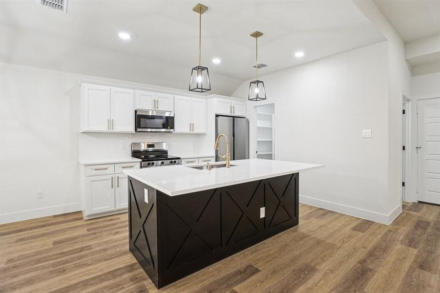 Kitchen with white cabinetry, an island with sink, appliances with stainless steel finishes, vaulted ceiling, and hanging light fixtures Kitchen with white cabinetry, an island with sink, appliances with stainless steel finishes, vaulted ceiling, and hanging light fixtures