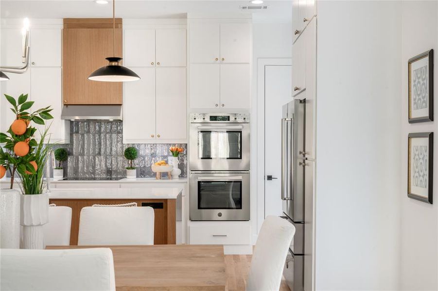 Kitchen with tasteful backsplash, white cabinets, extractor fan, appliances with stainless steel finishes, and decorative light fixtures