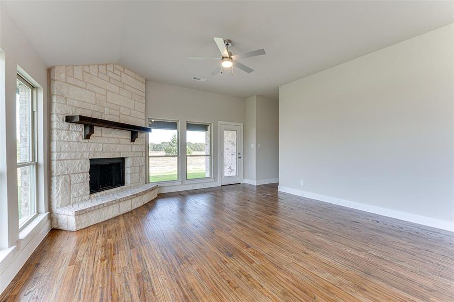 Unfurnished living room with ceiling fan, a fireplace, wood-type flooring, and vaulted ceiling