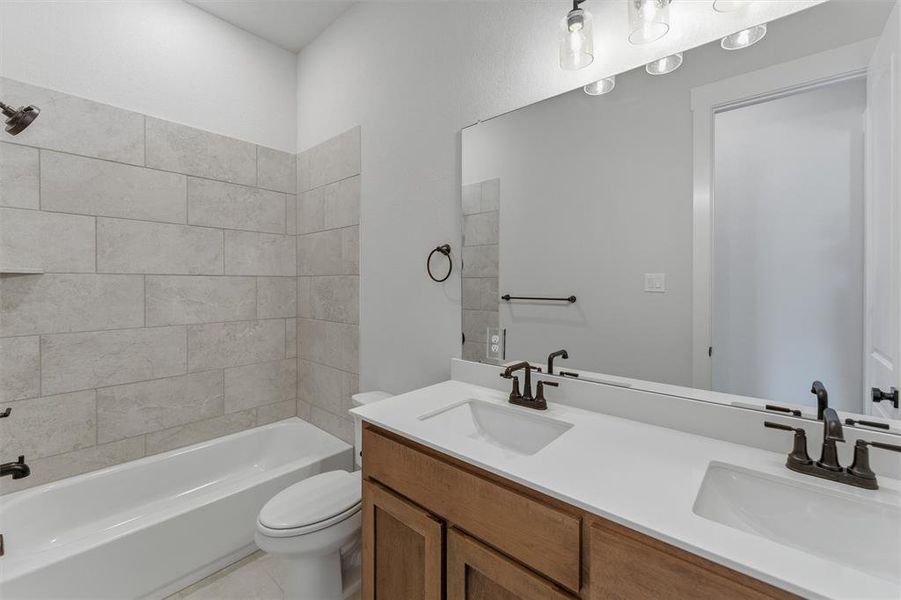 Bathroom featuring a dual vanity with a light wood-finish cabinet and white countertops, a large mirror, and a tub-shower combination with light-toned rectangular wall tile