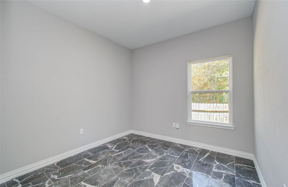 This room features sleek gray walls and a single window that offers natural light. The floor is finished with glossy, dark marble tiles, giving it a modern and elegant look.