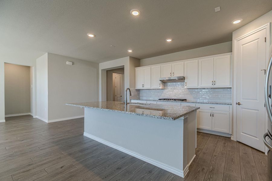 Kitchen featuring white cabinets, light stone countertops, tasteful backsplash, a center island with sink, and light wood finished floors Kitchen featuring white cabinets, light stone countertops, tasteful backsplash, a center island with sink, and light wood finished floors