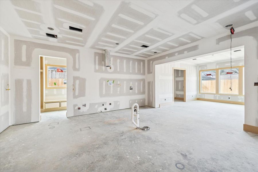 Open concept living anchored by a coffered ceiling detail and expansive wall space for custom cabinetry or statement finishes. Natural light pours in from the rear windows, creating seamless connection to the covered patio and backyard.