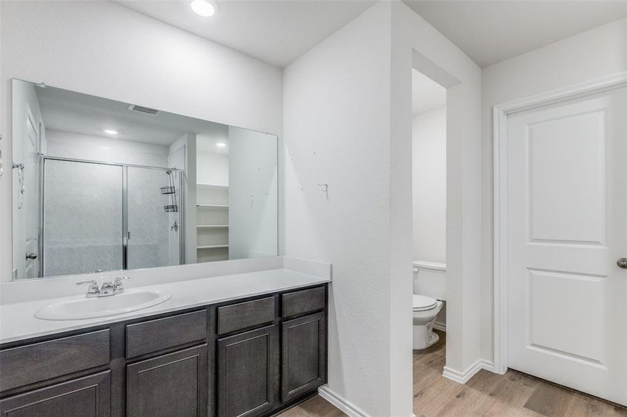 Bathroom with toilet, vanity, an enclosed shower, and hardwood / wood-style flooring