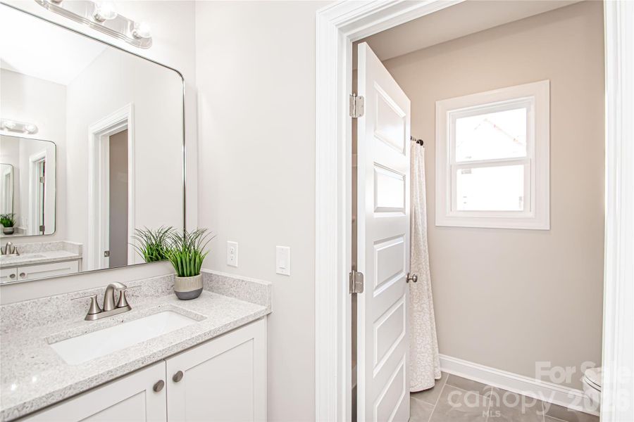 The hall bathroom boasts tile floors, dual white vanities, an oversized mirror, and brushed nickel fixtures and hardware for a clean, modern look.