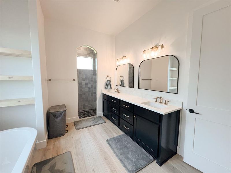Full bath featuring a walk in shower, double vanity, a soaking tub, and light wood-type flooring