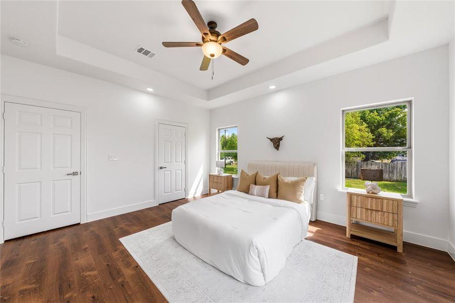 Spacious room featuring wood-finish flooring, a tray ceiling with a ceiling fan, recessed lighting, and two windows
