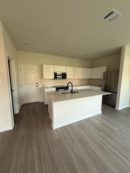 Kitchen with stainless steel appliances, white cabinetry, a center island with sink, light countertops, and dark wood-style floors Kitchen with stainless steel appliances, white cabinetry, a center island with sink, light countertops, and dark wood-style floors
