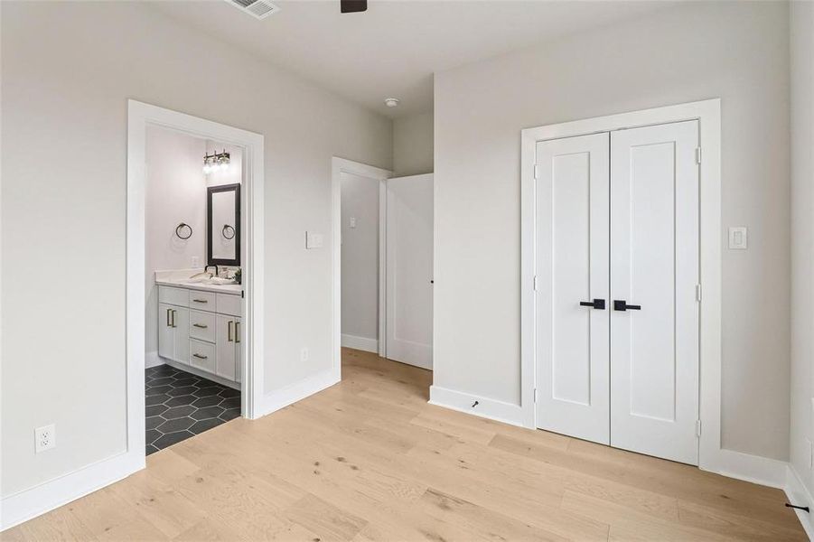 Light wood-finish flooring throughout, featuring a bathroom with hexagonal tile flooring, a white vanity with silver hardware, and a framed mirror