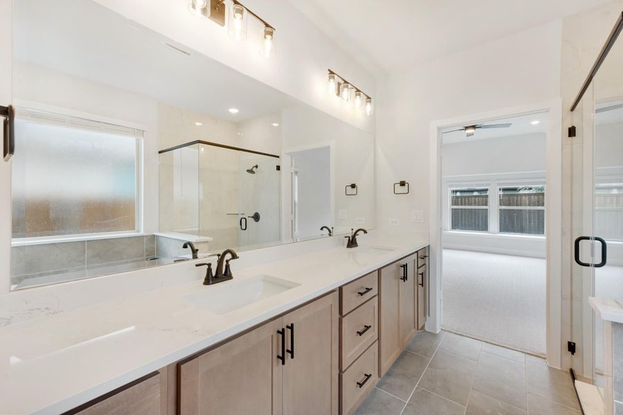 Master bathroom with double vanity, quartz countertops, glass shower, and tile floors