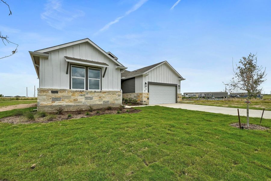 View of front of property with board and batten siding, stone siding, driveway, an attached garage, and a front lawn
