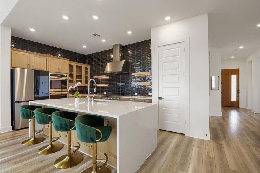 This contemporary kitchen features a spacious island with a breakfast bar, open shelving, but still plenty of cabinetry, drawers, and a pantry.