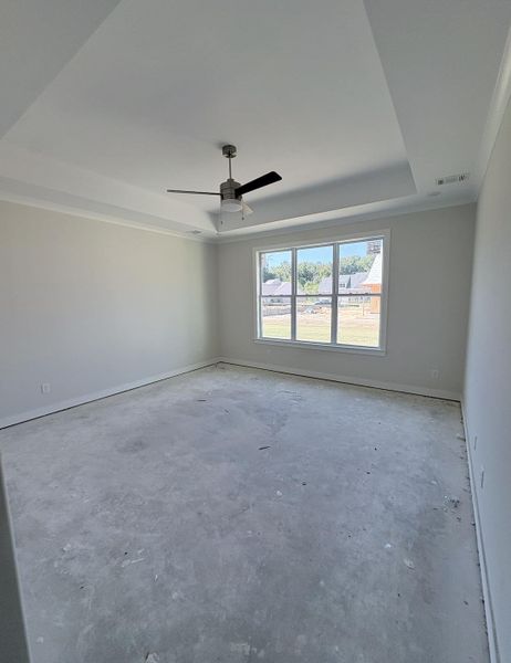 Tray ceiling with crown molding, ceiling fan with light fixture, large window, and light-toned wall paint Tray ceiling with crown molding, ceiling fan with light fixture, large window, and light-toned wall paint