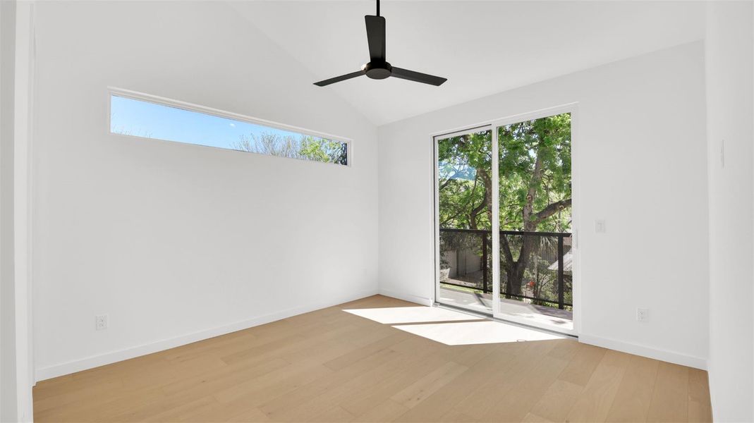 Bedroom featuring light wood-style flooring, vaulted ceiling, and a ceiling fan with attached bathroom and walk-in closet
