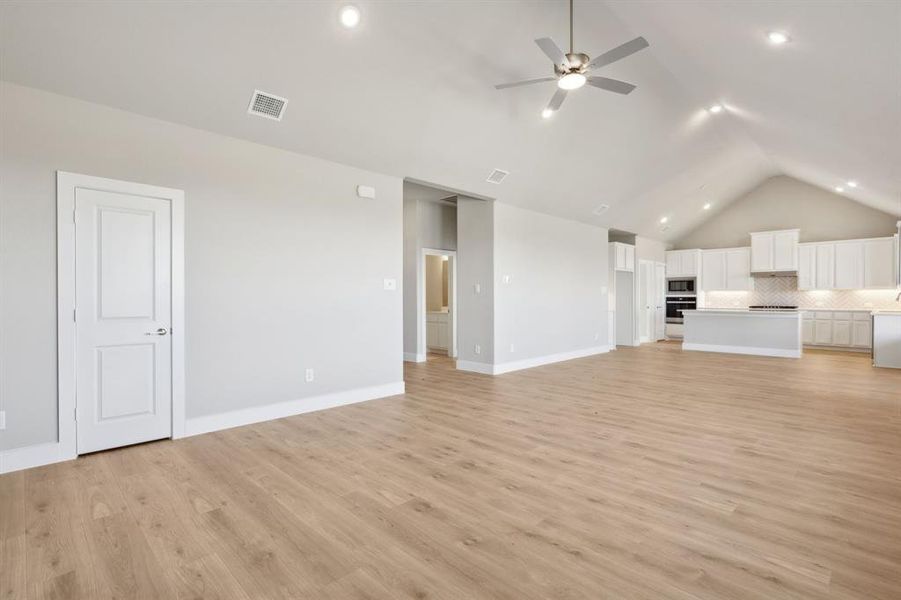 Unfurnished living room featuring ceiling fan, light hardwood / wood-style floors, and vaulted ceiling