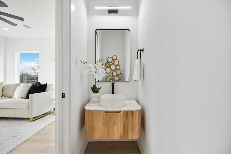 A sleek powder room showcases a modern floating wood-slat vanity with a round vessel sink, complemented by a tall black-framed mirror, contemporary lighting, and crisp white walls for a clean, minimalist look.