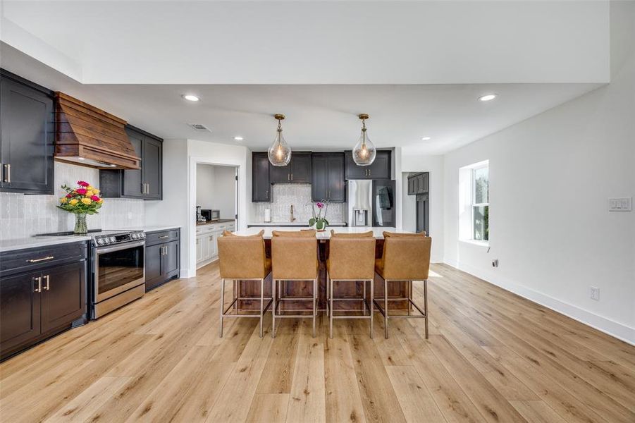 The kitchen features knotty alder kitchen island and vent hood, quartz counters, stainless steel appliances, pendant lighting, and ceramic tile.
