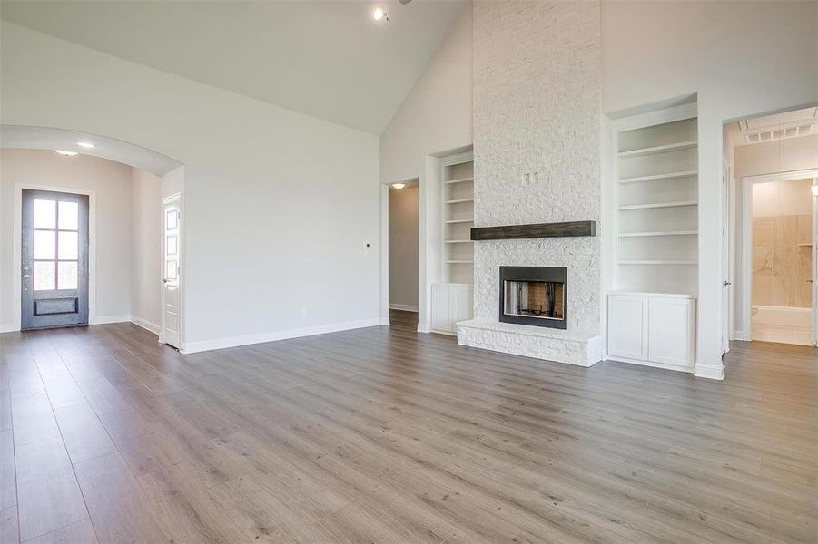 Unfurnished living room with light wood-type flooring, a fireplace, built in shelves, and high vaulted ceiling