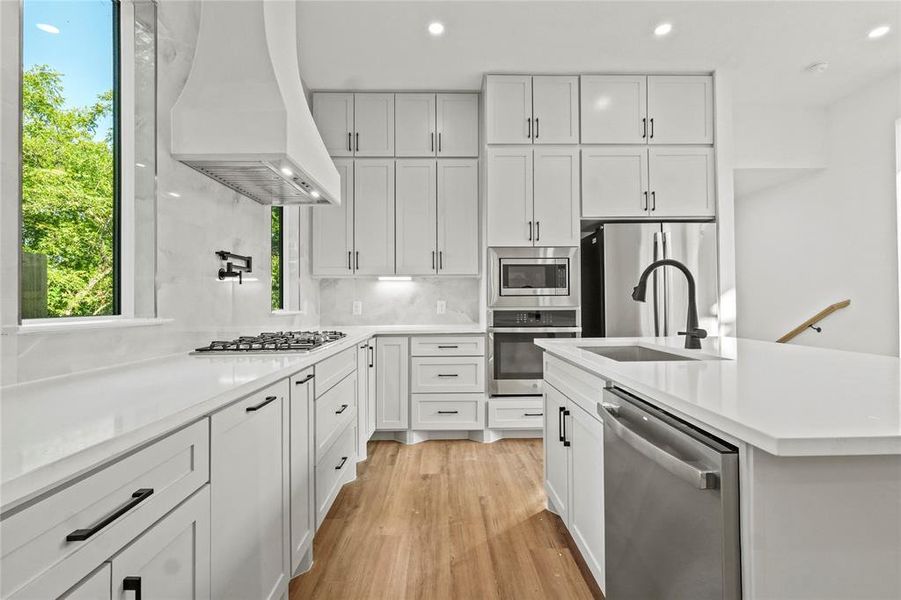 Kitchen with backsplash, custom exhaust hood, stainless steel appliances, recessed lighting, and light wood finished floors