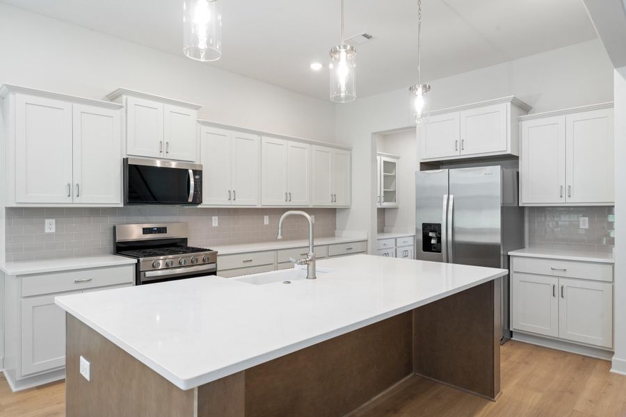 Kitchen featuring a large island with white countertop, subway tile backsplash, stainless steel appliances, and wood-finish flooring Kitchen featuring a large island with white countertop, subway tile backsplash, stainless steel appliances, and wood-finish flooring