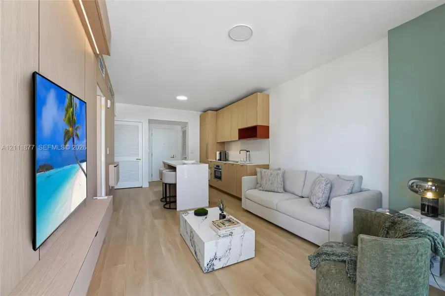 Light-toned wood-finish flooring, custom light-wood cabinetry, stone-finish kitchen island with built-in storage, and integrated accent lighting