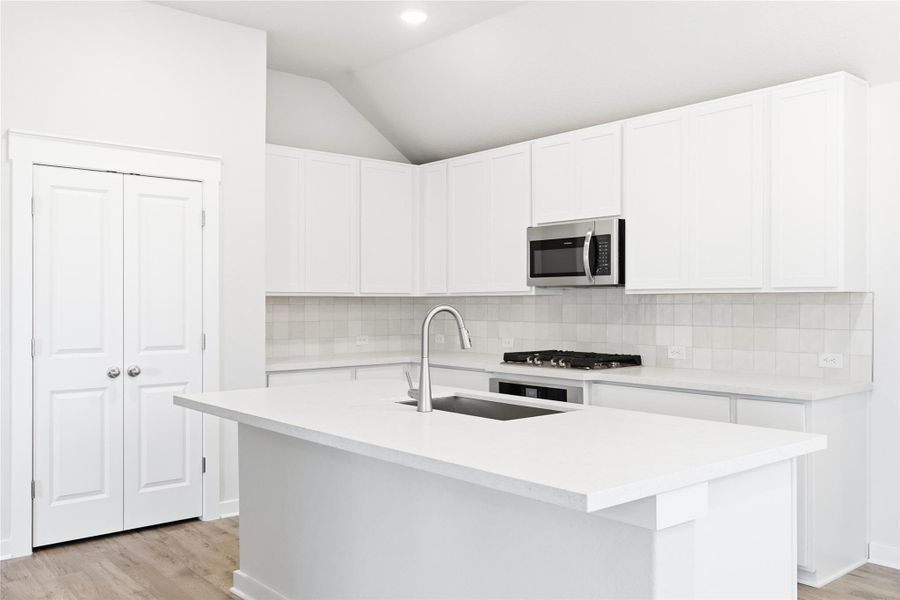 Kitchen with light wood finished floors, tasteful backsplash, a kitchen island with sink, lofted ceiling, and white cabinetry